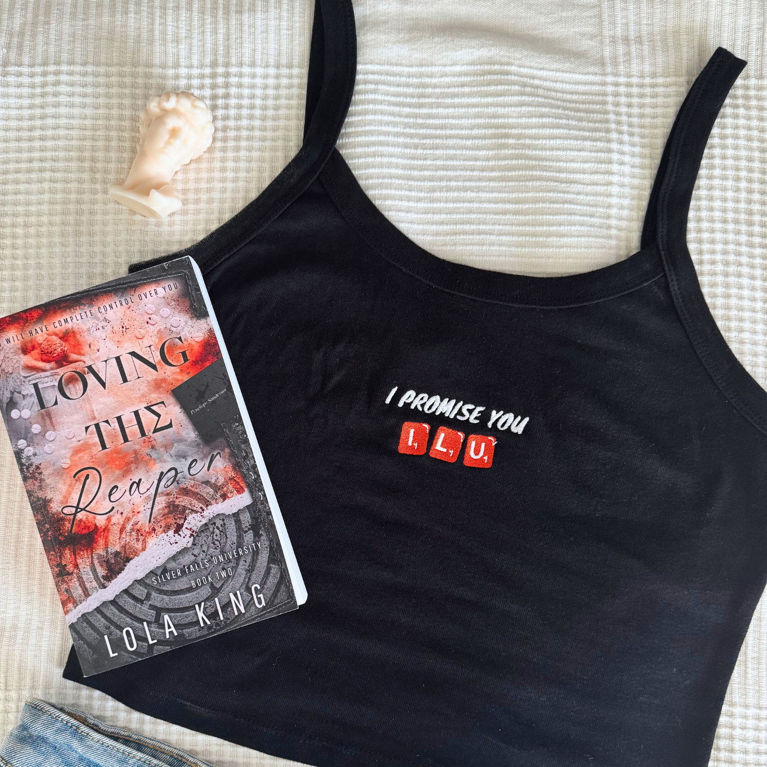 flay lay of a black tank top with the embroidery text "I promise you ILU scrabble stones. Together with the book Loving the Reaper by Lola King Merch