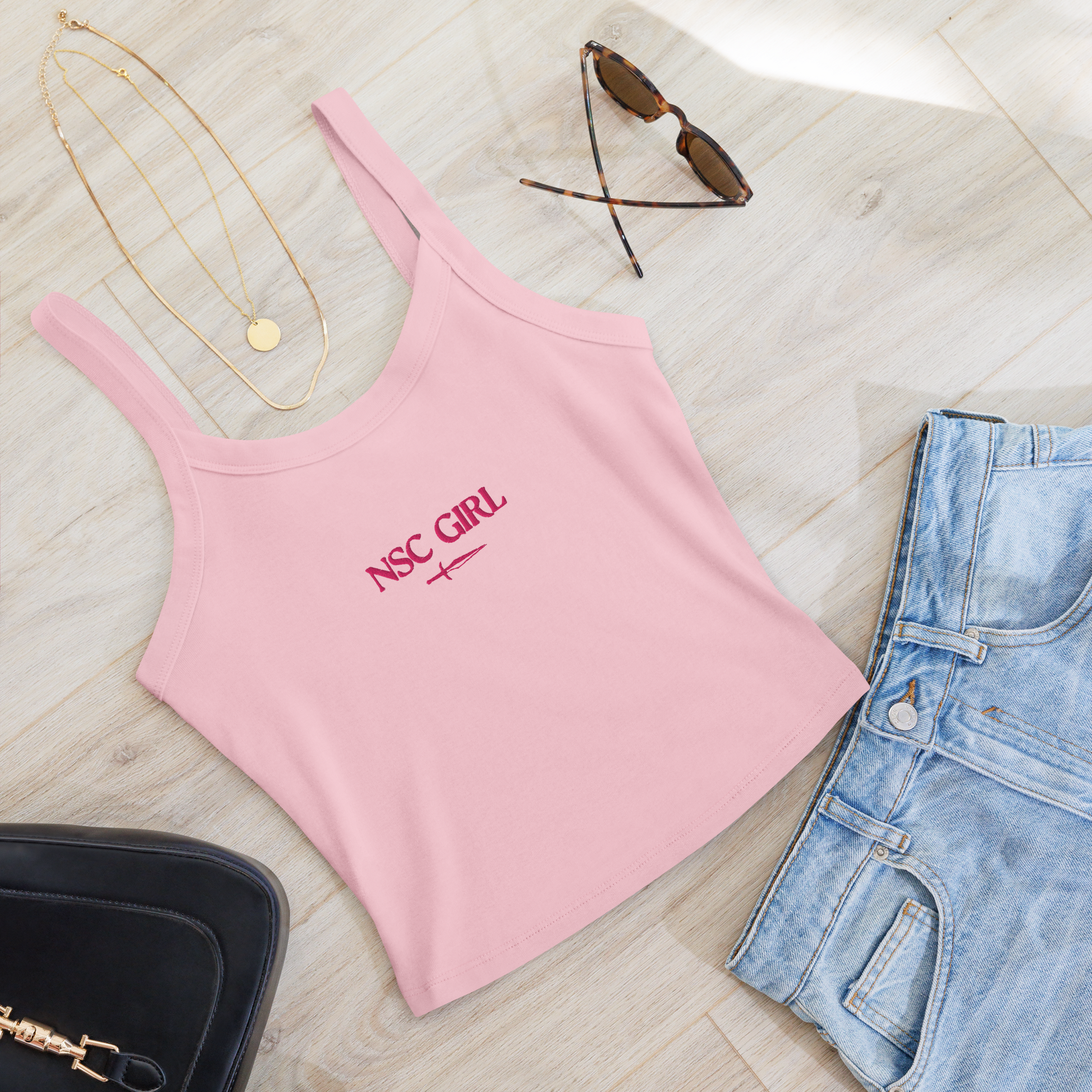 Flat lay of NSC Girl tank top with pink embroidery, styled with dark romance accessories and North Shore aesthetic